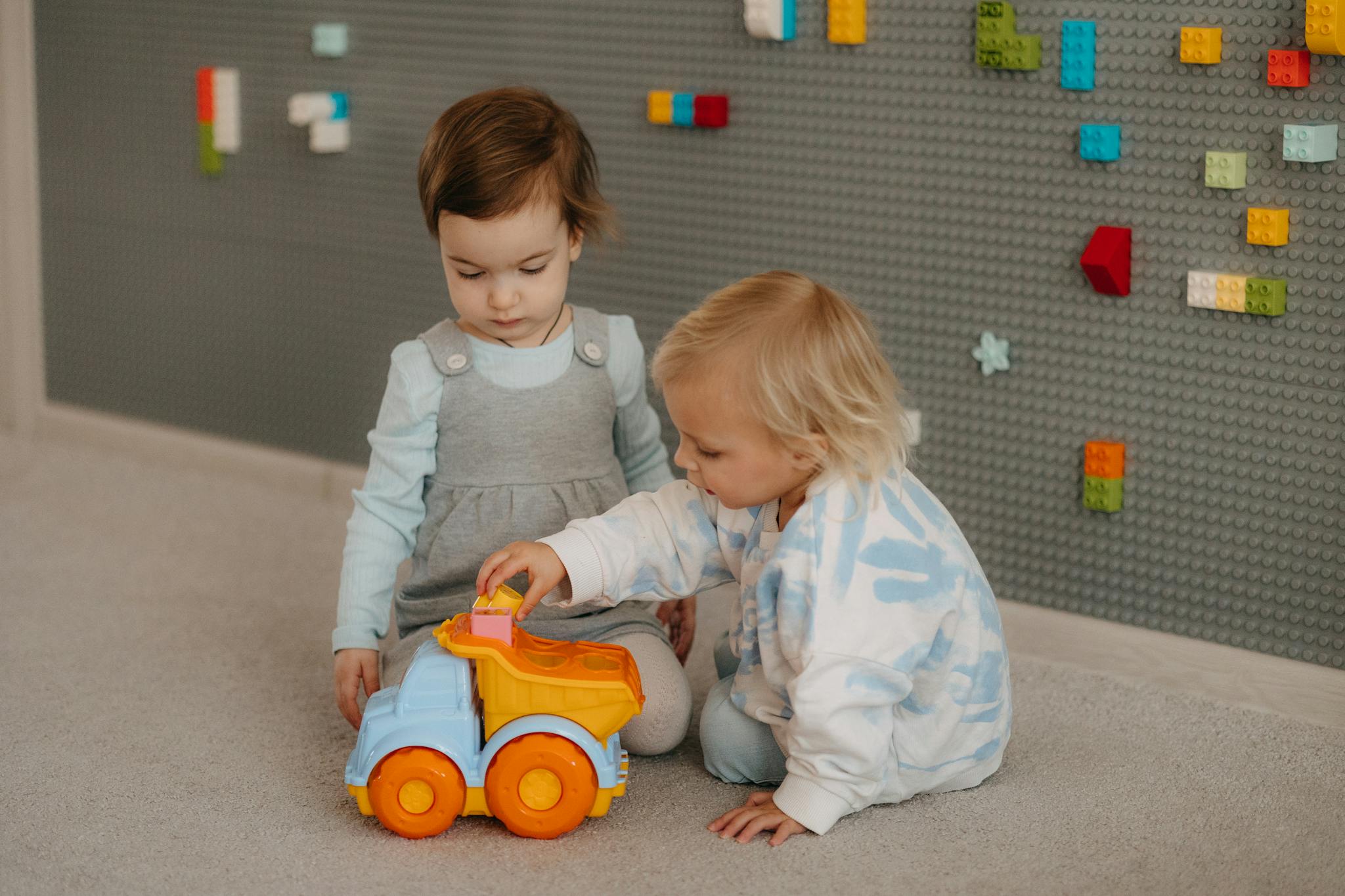 Two young children playing with a toy truck in a cozy indoor setting, exploring together.